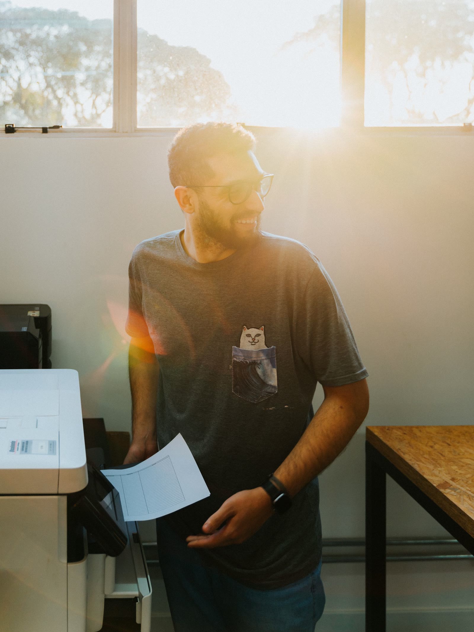 Une personne récupère un tirage à la sortie du multifonction, à contre-jour dans un bureau