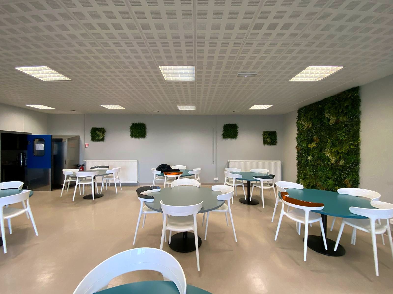 Cafétéria : tables rondes, chaises coque blanches et mur végétal