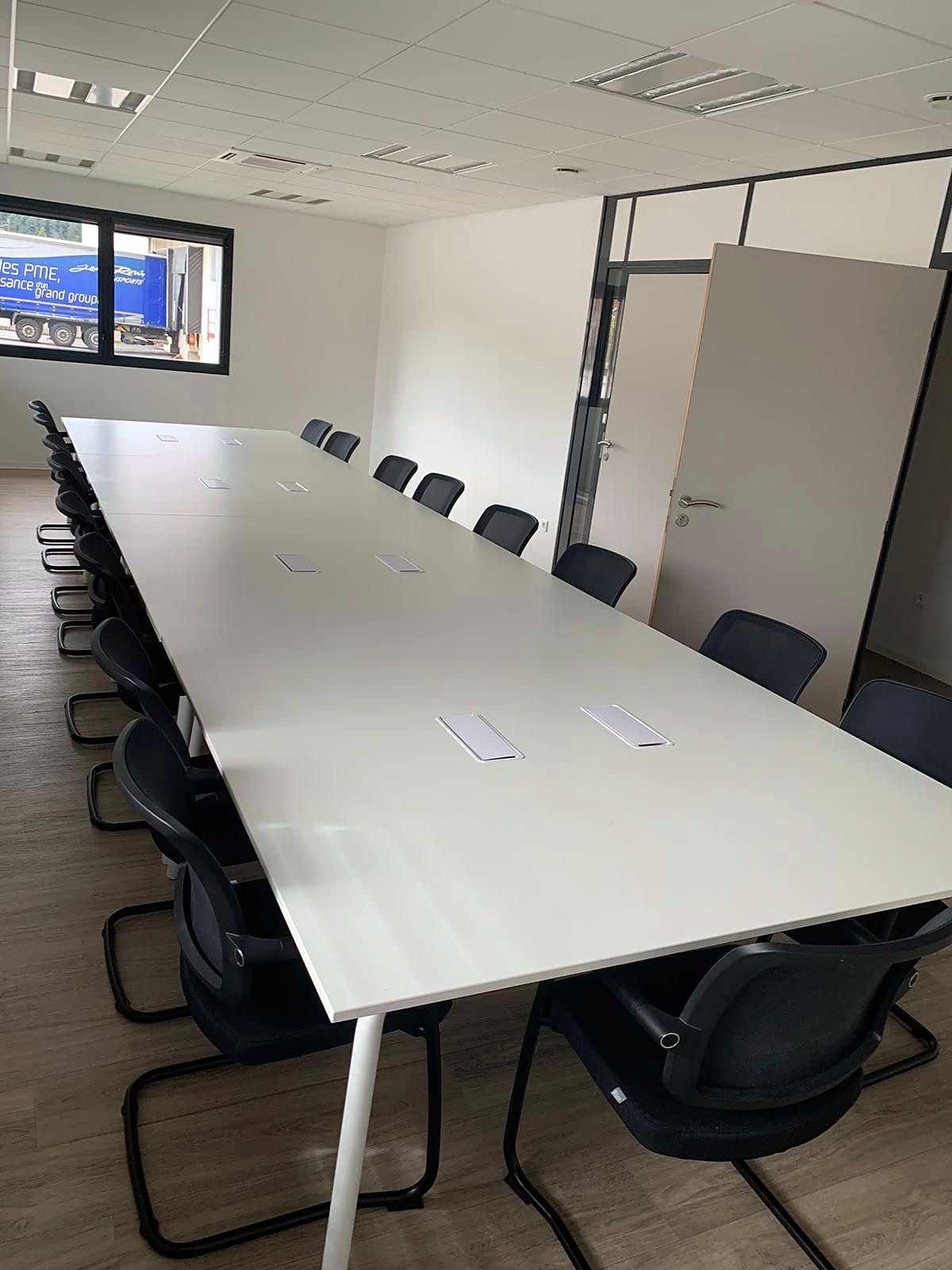 Salle de conseil&nbsp;: longue table blanche entourée de sièges luge noirs