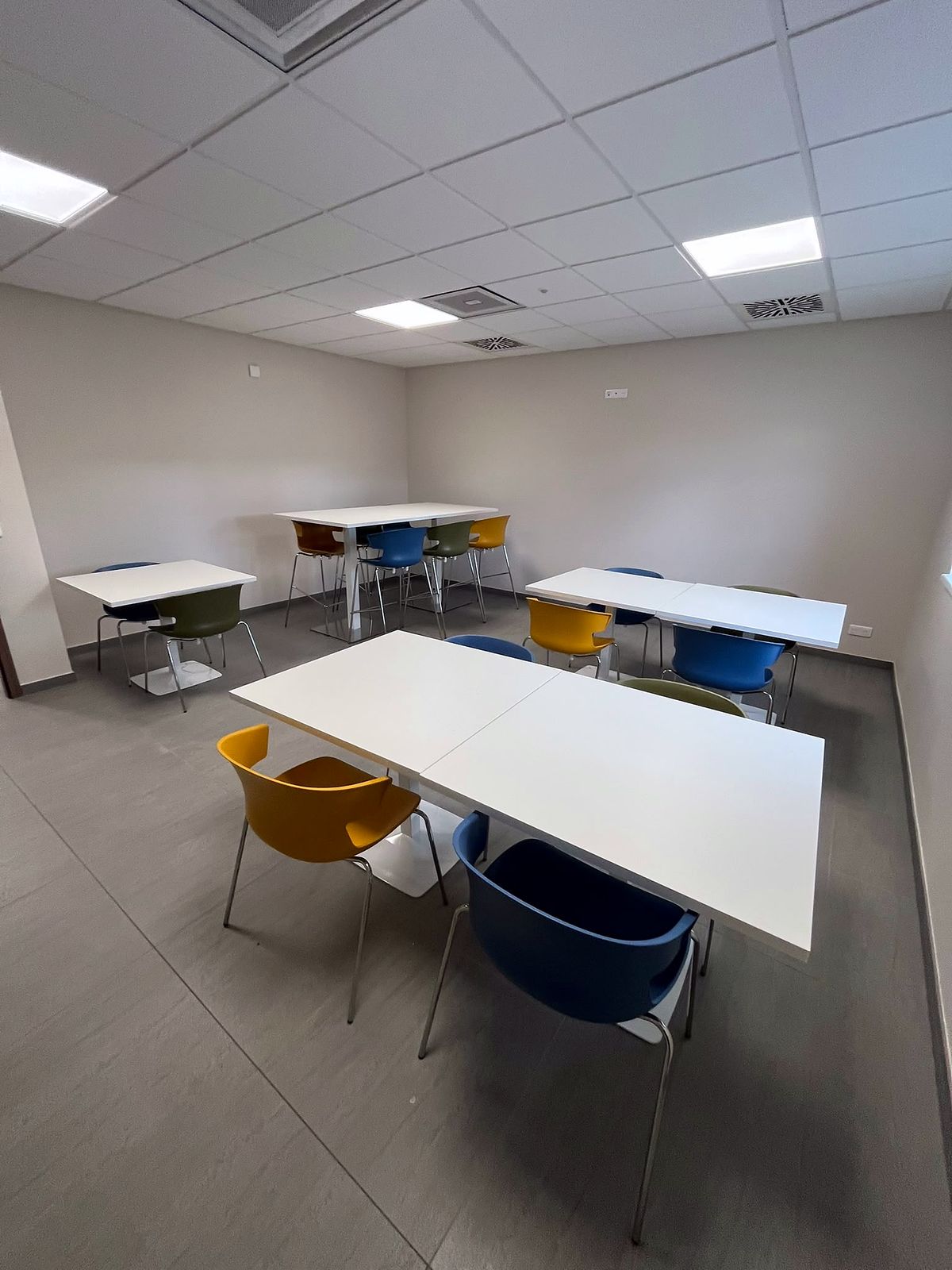 Salle de pause — Tables blanches et chaises coque de couleur, vue d’ensemble