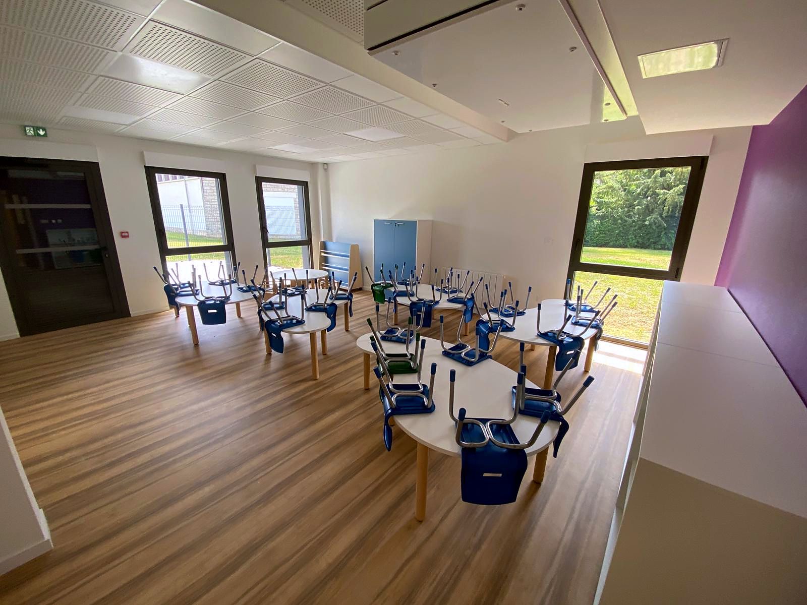 Salle polyvalente : tables rondes et chaises coque, rangées pour l’entretien