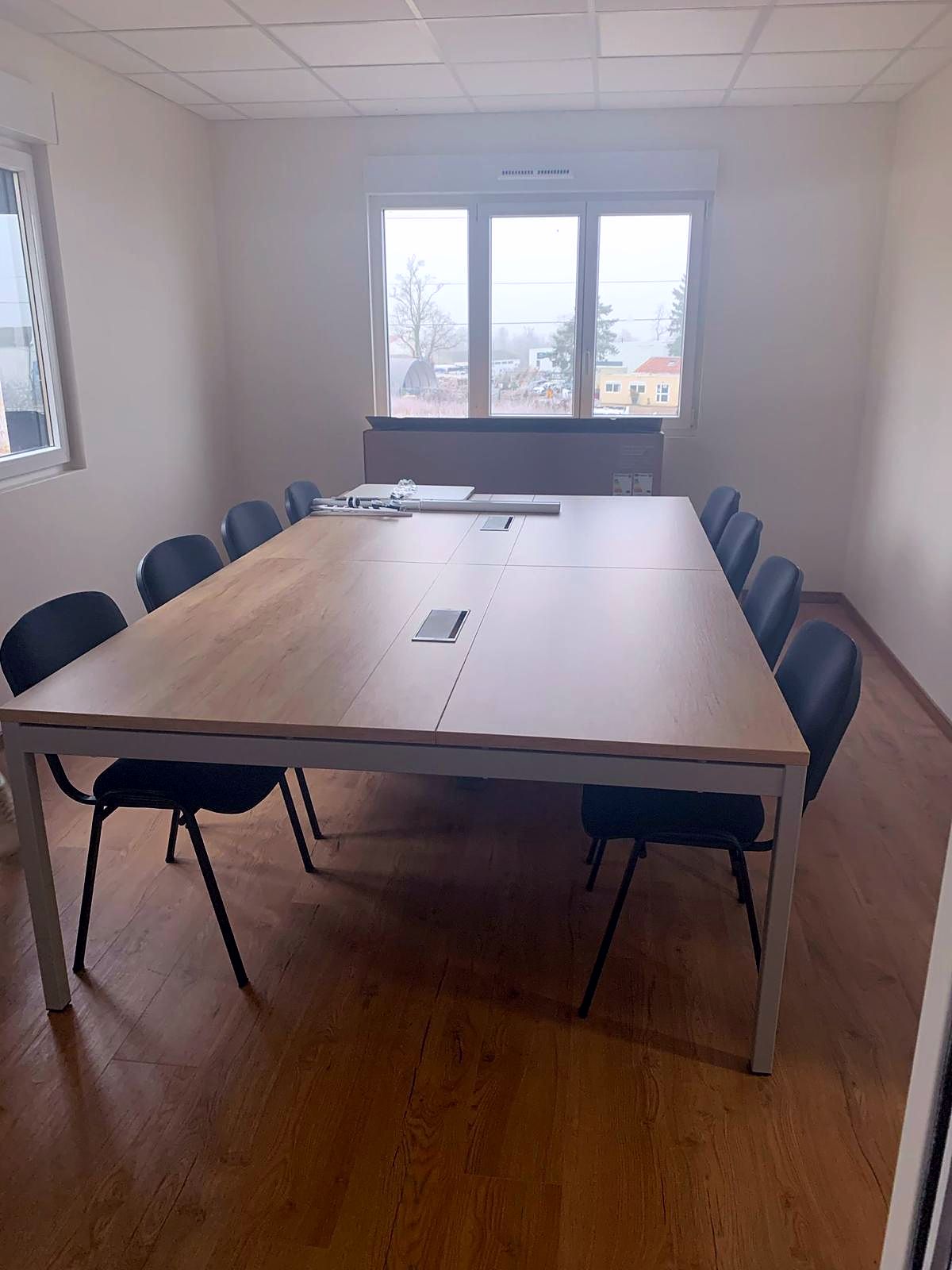 Salle de réunion : table chêne sur piètement blanc, chaises noires, lumière naturelle