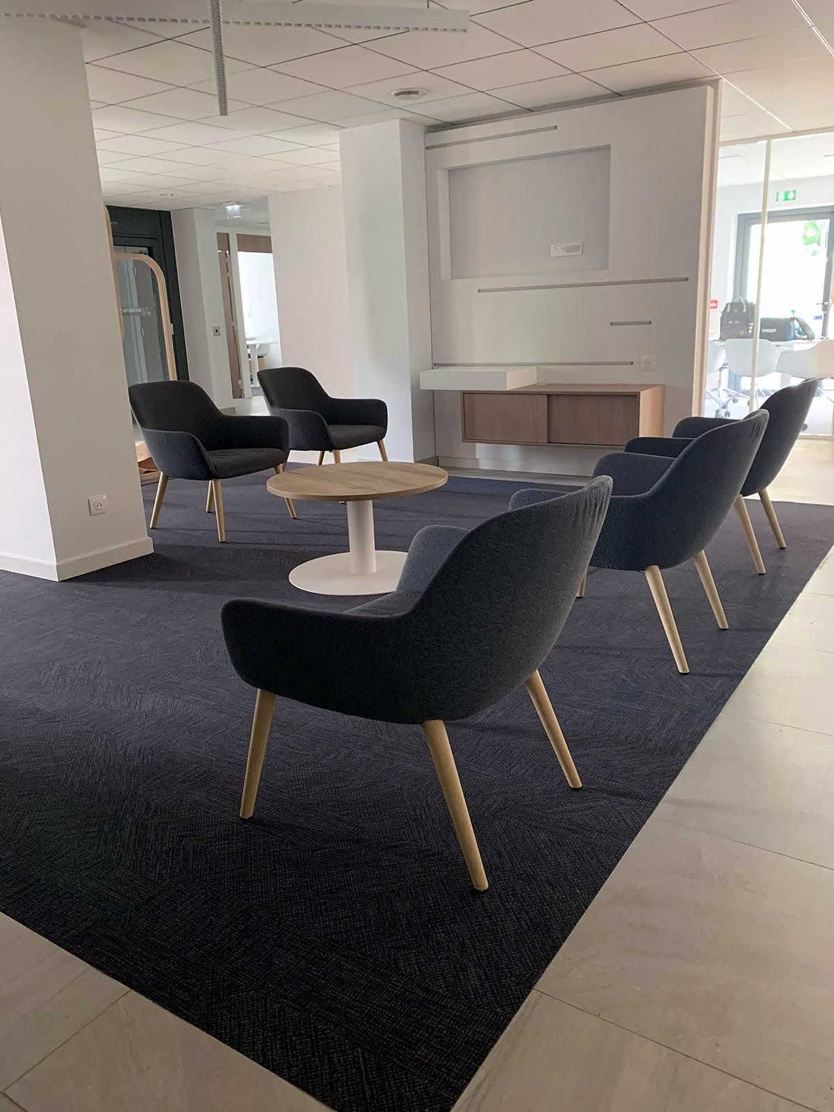 Salon d’attente : fauteuils enveloppants gris, table basse bois et tapis